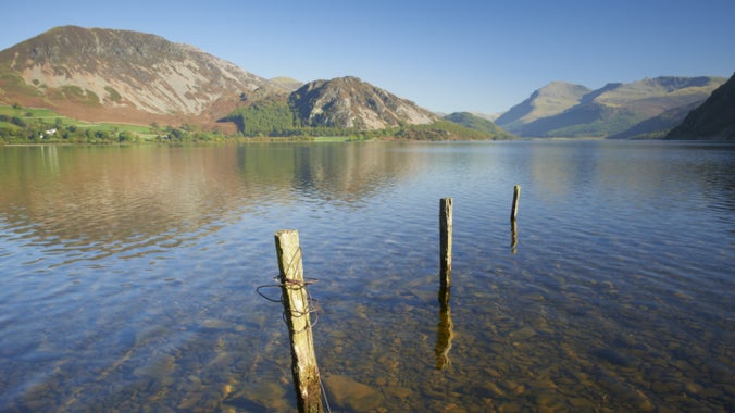 A view of the fells from the Ennerdale Water shoreline, Cumbria, showing the calm water and clear blue sky.